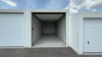 Offene Garagenbox mit weißem Sektionaltor und asphaltiertem Vorplatz unter blauem Himmel.