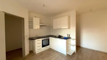 Moderne Einbauküche mit weißen Schränken, dunkler Arbeitsplatte und integriertem Backofen in einem offenen Wohnbereich.