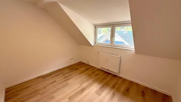Helles Zimmer im Dachgeschoss mit Laminatboden, schrägen Wänden und Fenster mit Ausblick.
