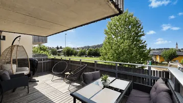 Geräumiger Balkon mit Holzboden, bequemen Loungemöbeln und weitem Blick ins Grüne.