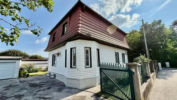 Traditionelles Einfamilienhaus mit Mansarddach, weißer Fassade und grünem Gartentor.