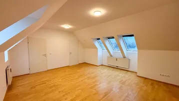 Geräumiges Zimmer im Dachgeschoss mit Holzboden, schrägen Wänden und drei Dachfenstern für viel Licht.