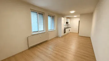 Heller offener Wohnbereich mit integrierter Küchenzeile und Laminatboden, bereit zur individuellen Gestaltung.