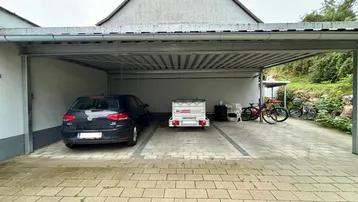 Geräumiger Carport mit Platz für ein Auto und Fahrräder, angrenzend an das Gebäude.