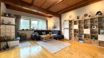 Gemütliches Wohnzimmer mit Holzbalkendecke, Kachelofen und Blick ins Grüne.