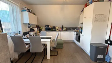 Moderne Küche mit weißen Schränken und Essbereich unter einer Dachschräge, ausgestattet mit Holzboden.