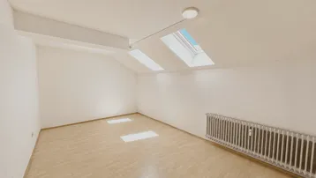 Heller Raum im Dachgeschoss mit Laminatboden, Dachschrägen und zwei Dachfenstern für natürliches Licht.