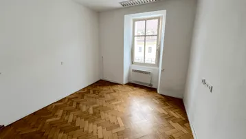 Heller Raum mit Fischgrätparkettboden und einem Fenster, das Tageslicht hereinlässt.