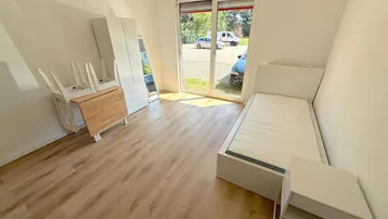 Helles Schlafzimmer mit Laminatboden, großem Fenster und Blick ins Grüne.