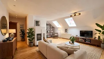 Gemütliches Wohnzimmer im Dachgeschoss mit Kamin, Holzboden und zwei Dachfenstern für viel Licht.