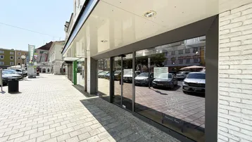 Nahaufnahme der Glasfront eines Geschäftsgebäudes mit reflektierenden Autos und einem Bürgersteig.