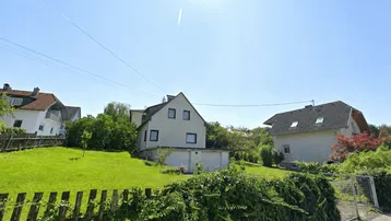 Ansicht eines Einfamilienhauses mit großem Garten und Holzzaun unter blauem Himmel.