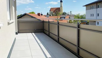 Heller Balkon mit Fliesenboden und Blick auf die Kirche unter blauem Himmel.
