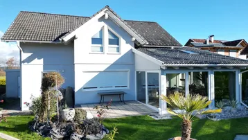 Ansicht des Hauses mit Wintergarten, Terrasse und gepflegtem Garten unter blauem Himmel.