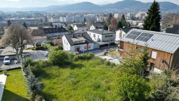 Blick über eine grüne Wiese auf eine Wohnsiedlung mit modernen Häusern und Bergblick.