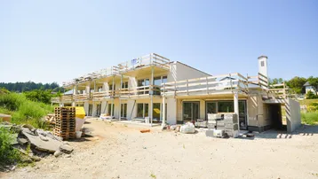 Neubauprojekt mit mehreren Balkonen in der Bauphase, umgeben von Natur und Baustellenmaterialien.