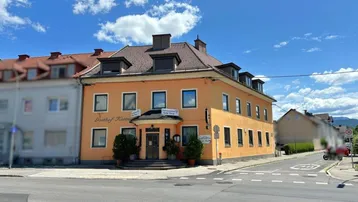 Gebäudeansicht eines Gasthofs an einer Straßenecke mit orangefarbener Fassade und mehreren Fenstern.
