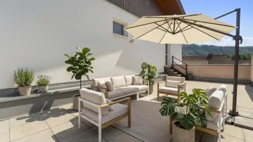 Große, sonnige Terrasse mit bequemen Gartenmöbeln und Sonnenschirm, ideal zum Entspannen.