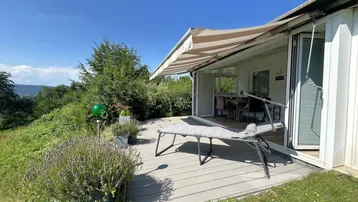 Geräumige Terrasse mit Sonnenliege und Markise, umgeben von grüner Natur und weitem Ausblick.