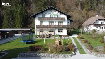 Traditionelles Haus Moser mit Balkonen, Spielplatz und Carport in ländlicher Umgebung.