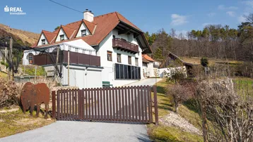 Traditionelles Landhaus mit Satteldach und Holztor, umgeben von ländlicher Natur.