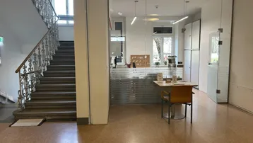 Geräumiger Eingangsbereich mit Treppenhaus und einem durch Glaswände abgetrennten Bürobereich.
