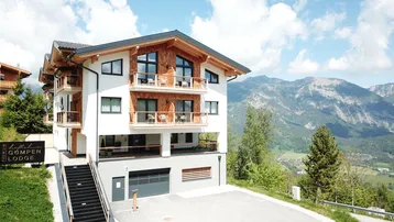 Modernes Chalet mit Holzfassade und Balkonen, eingebettet in eine Berglandschaft mit weitem Blick.