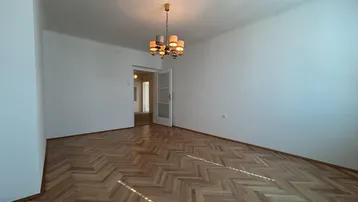 Geräumiges, leeres Zimmer mit Fischgrätparkett und Kronleuchter, bereit zur individuellen Gestaltung.