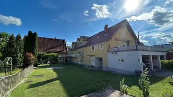 Großer, gepflegter Gartenbereich hinter dem Gebäude mit sonniger Rasenfläche und altem Baumbestand.