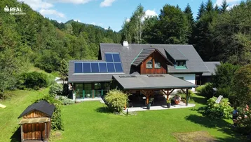 Luftaufnahme des Hauses mit großem Garten, Photovoltaikanlage auf dem Dach und umgebender Natur.