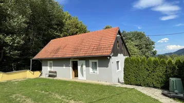 Kleines Haus mit rotem Ziegeldach und gepflegtem Rasen in ländlicher Umgebung.