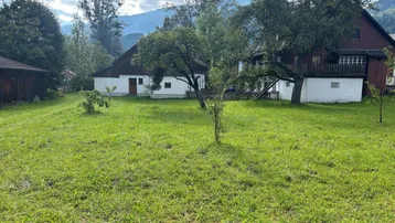 Großer Garten mit weitläufiger Rasenfläche, umgeben von Bäumen und traditionellen Häusern, mit Bergblick im Hintergrund.