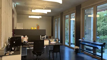 Modernes Büro mit Sichtbetondecke, großen Fenstern und Blick ins Grüne.