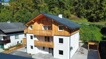 Neubau im alpinen Stil mit Holzfassade und Balkonen, umgeben von grüner Natur.