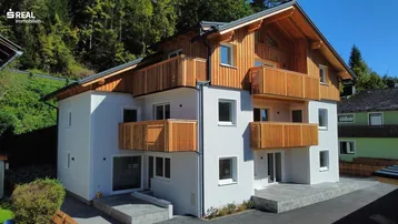 Modernes Mehrfamilienhaus mit Holzverkleidung und Balkonen in alpiner Umgebung.