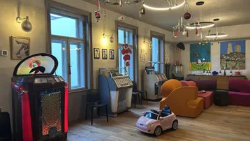 Geräumiger Wohnbereich mit mehreren Jukeboxen, modernen Leuchten und Holzparkettboden.