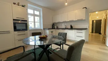 Moderne Wohnküche mit weißen Schränken, dunkler Arbeitsplatte und Esstisch am Fenster.