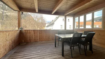 Überdachte Holzterrasse mit Esstisch und Stühlen, bietet einen weiten Blick auf die Berge.