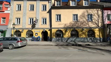 Historisches Gebäude mit gelber Fassade und traditioneller Architektur an einer belebten Straße mit parkenden Autos.