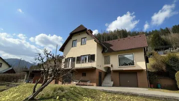 Traditionelles Einfamilienhaus mit Satteldach und Balkon in ländlicher Umgebung mit Bergblick.