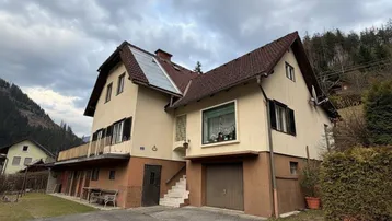 Ansicht des Hauses mit Satteldach und Photovoltaikanlage auf dem Dach in bergiger Landschaft.