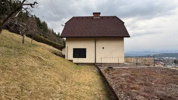 Seitenansicht des Hauses mit weitem Blick über die Landschaft und angrenzendem Hang.
