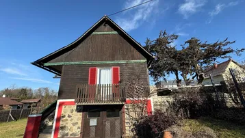 Traditionelles Holzhaus mit Steinsockel, kleinem Balkon und Satteldach.