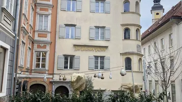 Historisches Gebäude in der Altstadt mit traditionellen Fensterläden und einem Glockenturm im Hintergrund.