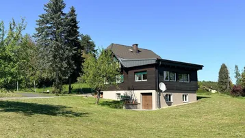 Rückansicht des Holzhauses mit Satteldach, Garage im Untergeschoss und weitem Blick ins Grüne.