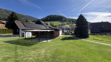 Geräumiger Gartenbereich mit Carport und Blick auf die bewaldeten Hügel und Berge.