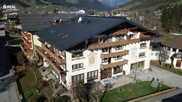 Traditionelles Mehrfamilienhaus mit Holzverkleidung und Balkonen in alpiner Umgebung.