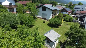 Weitläufiger Gartenbereich mit Rasenfläche, Bäumen und einem kleinen Gartenhaus, umgeben von Natur.