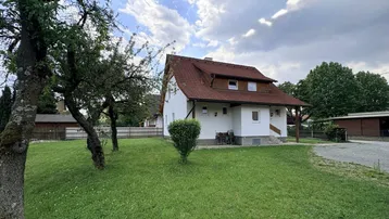 Freistehendes Einfamilienhaus mit großem Garten und altem Baumbestand unter bewölktem Himmel.