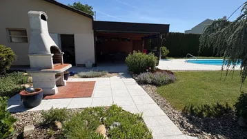 Großer Gartenbereich mit Außenkamin, gepflasterten Wegen, einem Pool und überdachtem Sitzbereich.